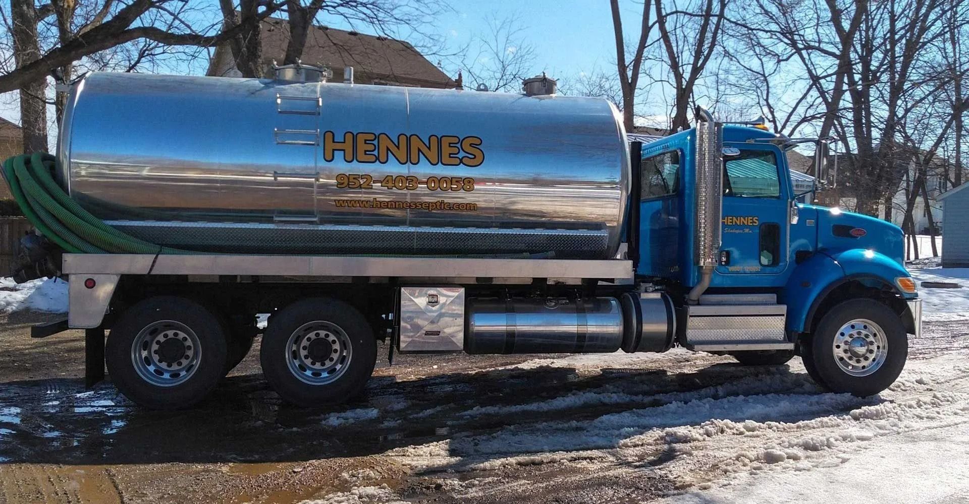 Blue septic truck with a shiny silver tank, parked on a snowy area. 