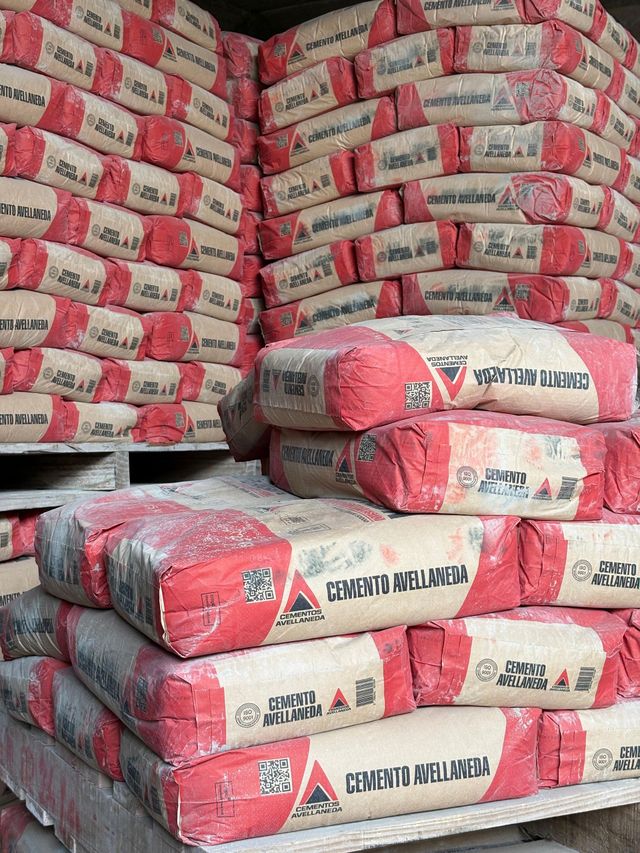 Palés de ladrillo rojo apilados y envueltos en plástico junto a una carretilla elevadora en el patio de un almacén.