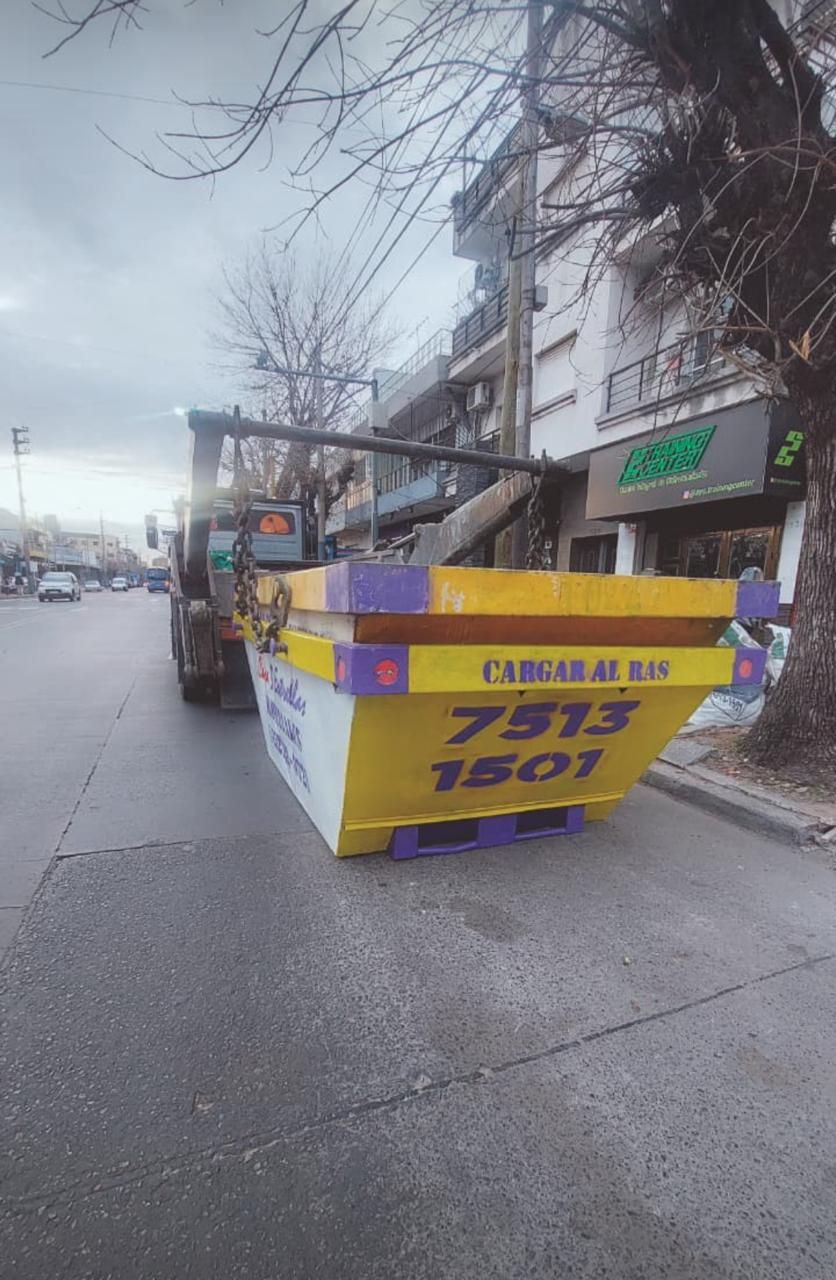 Camión de reparto naranja descargando materiales de construcción en una obra con un trabajador con chaleco de seguridad.