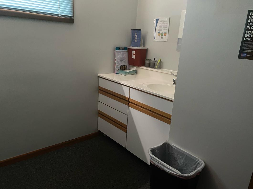 A white bathroom vanity with drawers and a sink, sitting in the corner of a room with gray walls and carpet.