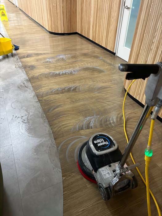 A floor buffer machine cleaning a wooden hallway floor with circular marks visible on the surface.