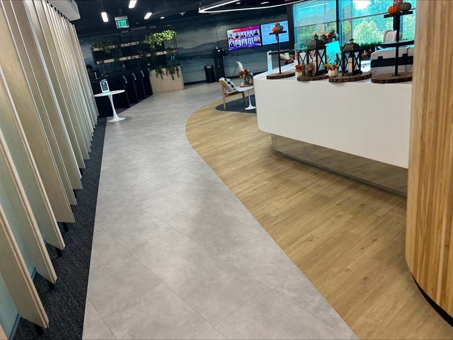 A modern office interior featuring a curved floor transition from grey tile to wood-look planks near a white reception desk.