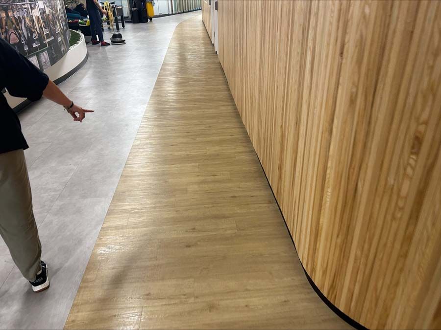 A person pointing toward a wooden walkway next to a curved, slatted wood-paneled wall in a modern building.