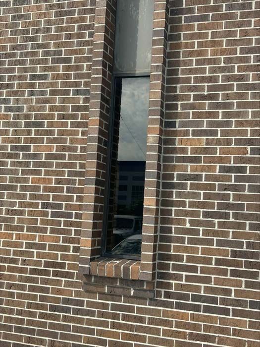 A narrow, vertical rectangular window set into a wall made of multi-toned brown and tan bricks.