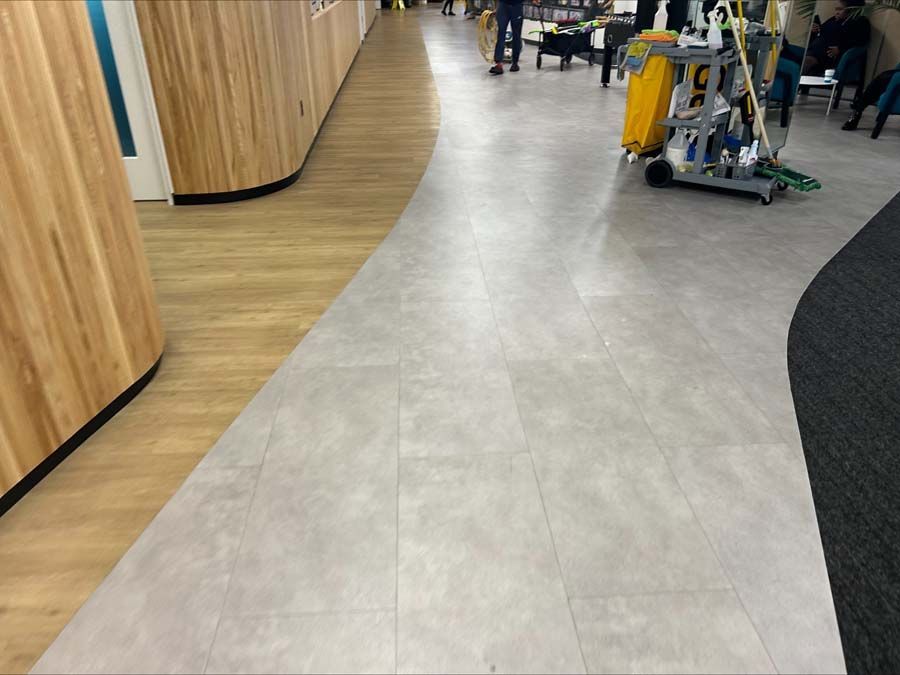 A hallway with wood-paneled walls, gray tiled flooring, and a rolling cleaning cart in a modern public space.