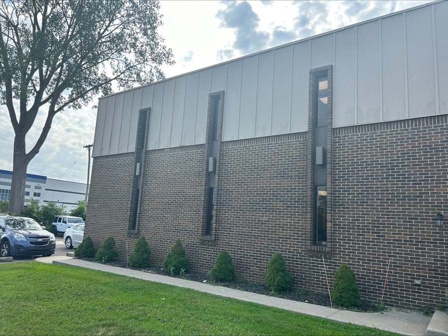 Exterior side view of a building with a brick lower level, metal upper siding, and three tall vertical windows.