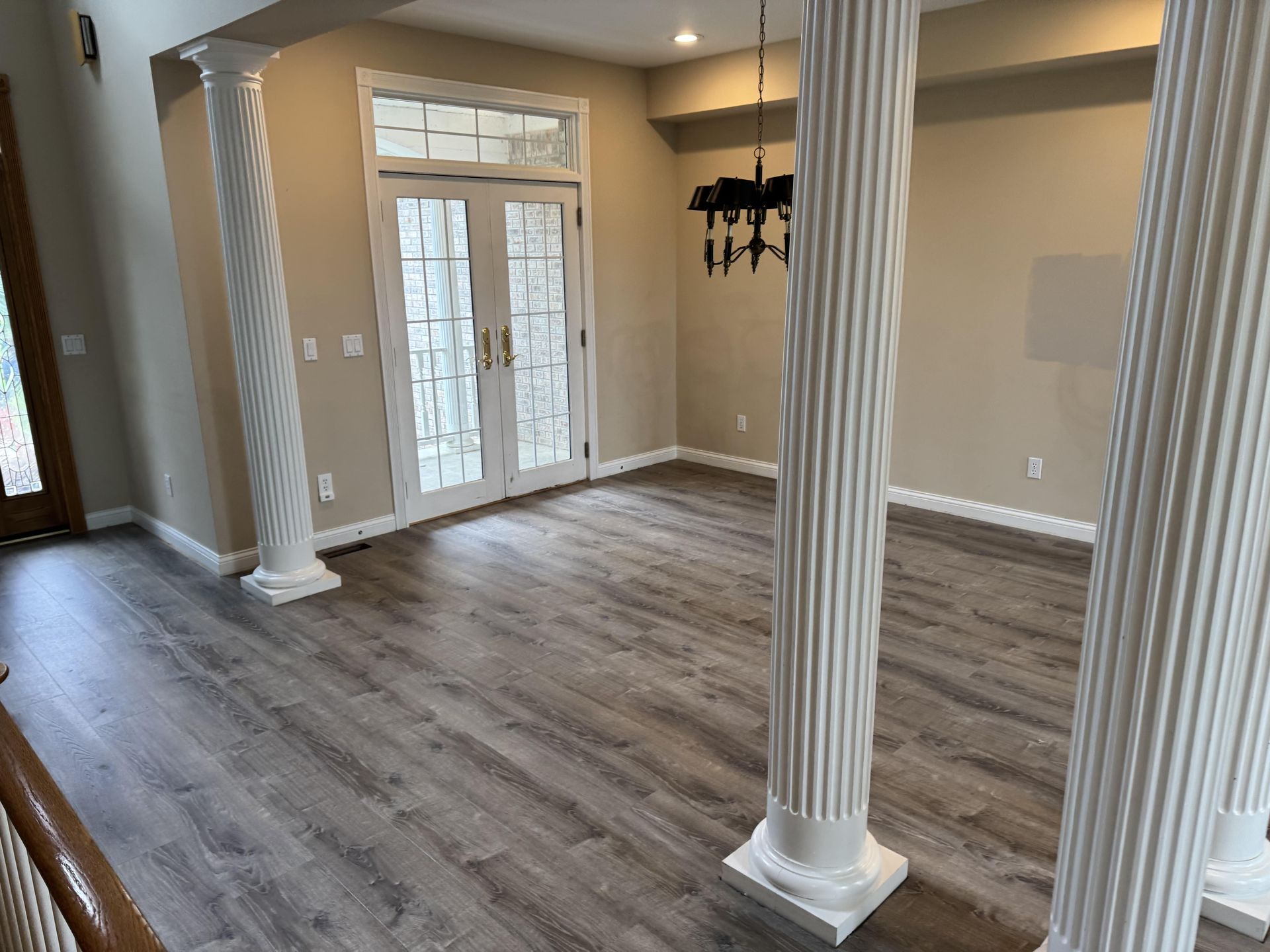 A room with light brown wood-look flooring, white fluted columns, and a set of glass-paneled double doors.