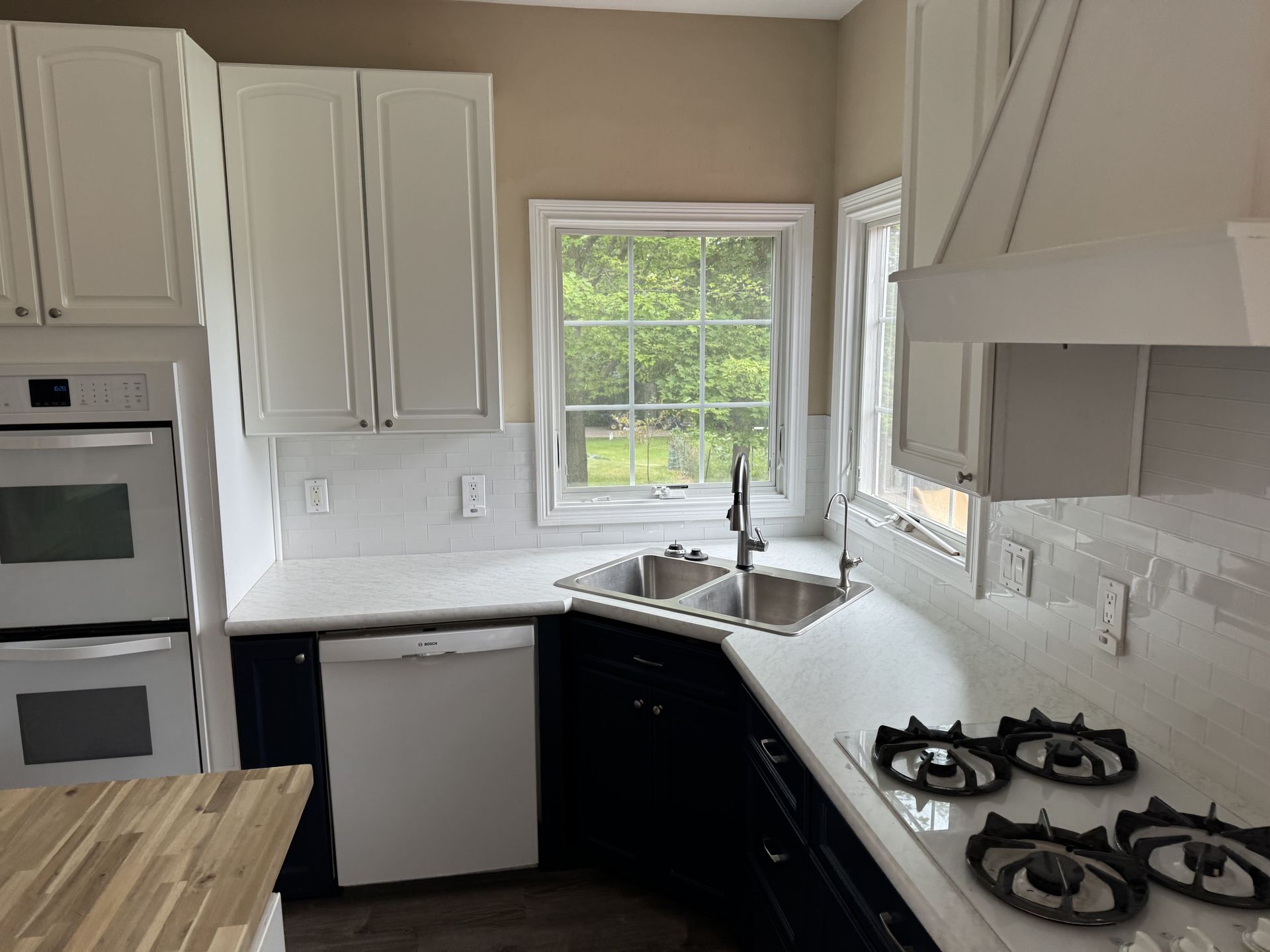 A modern kitchen with white cabinets, dark lower cabinets, white countertops, a double wall oven, and a gas cooktop.