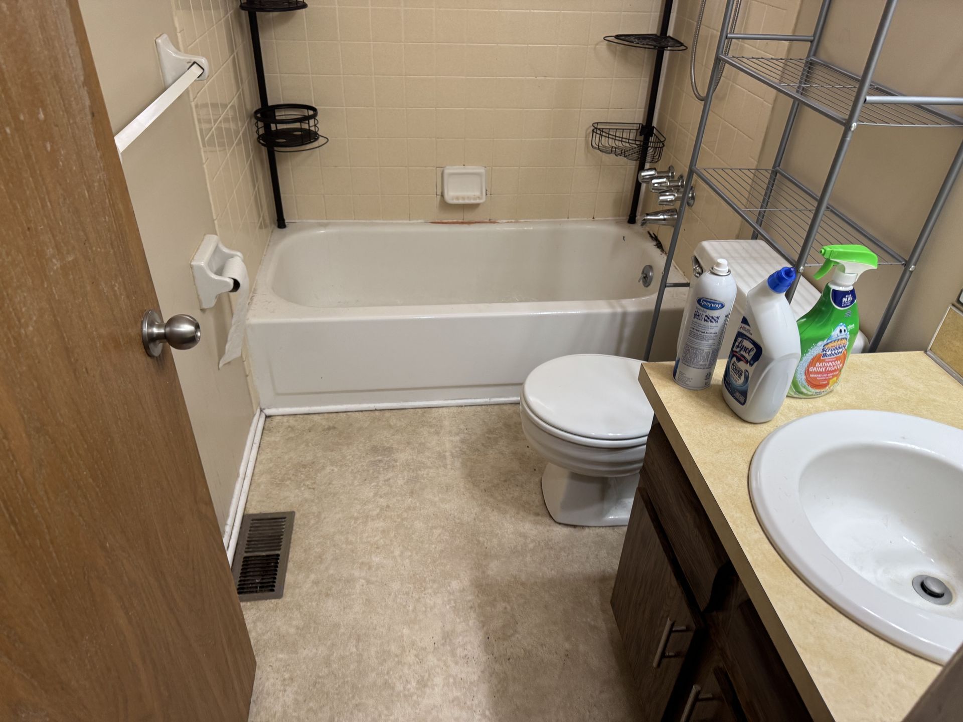 A small, neutral-toned bathroom with a tub, toilet, vanity sink, and wire shelving.