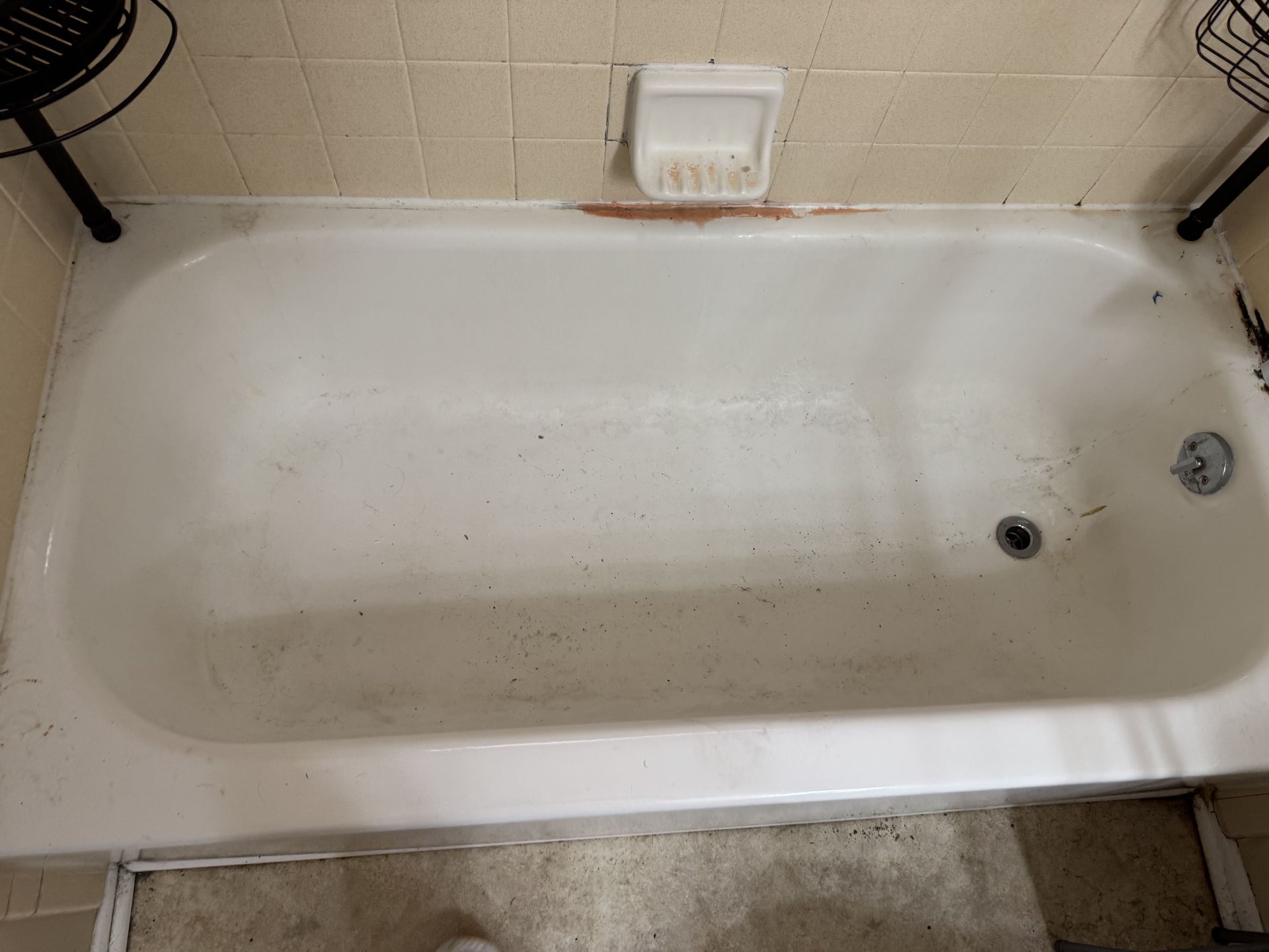 A white, rectangular bathtub with a soap dish on the tiled wall above and metal shower racks on either side.