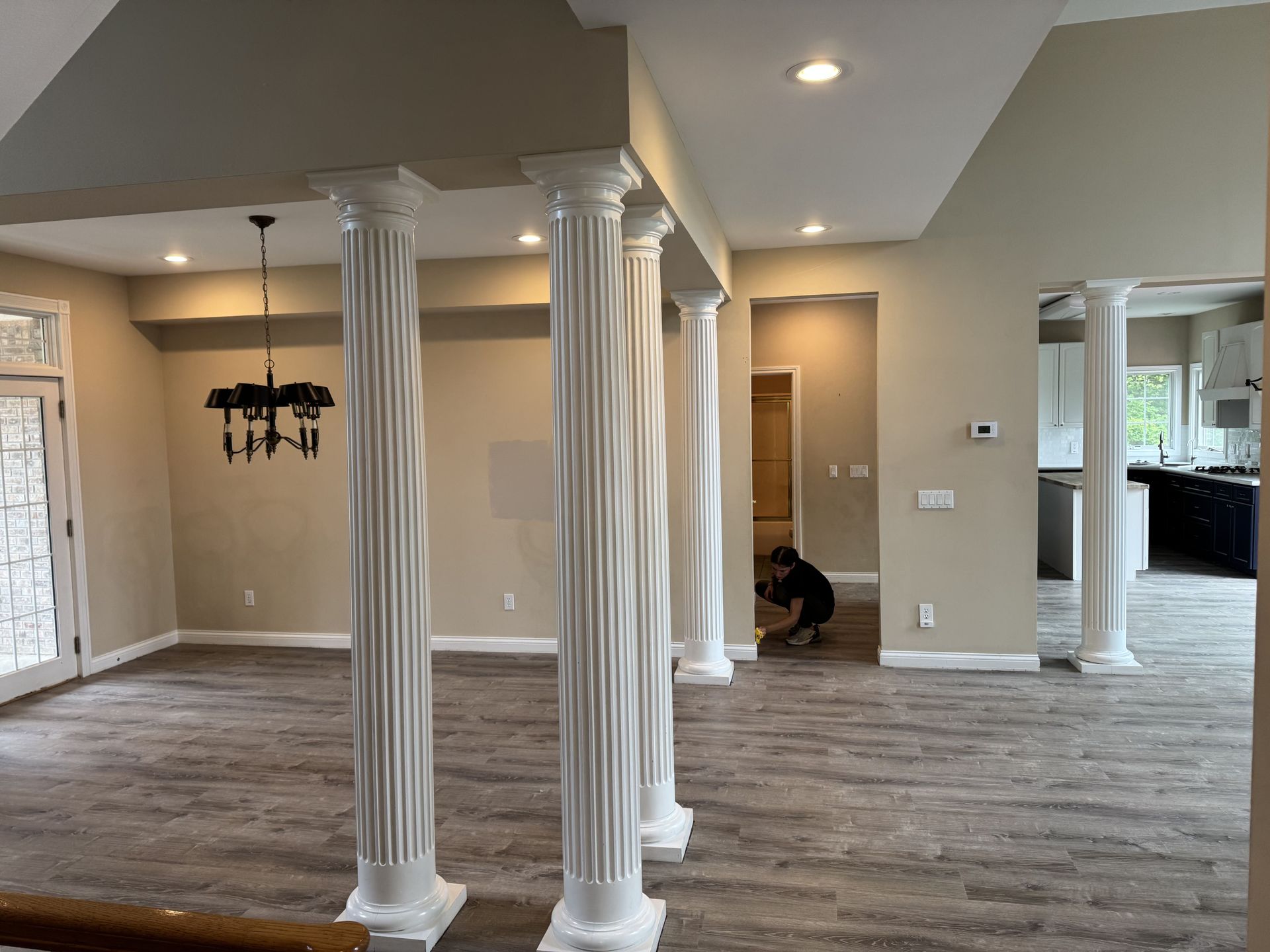An open-concept living area with white fluted columns, light wood-look flooring, and a dining room with a chandelier.
