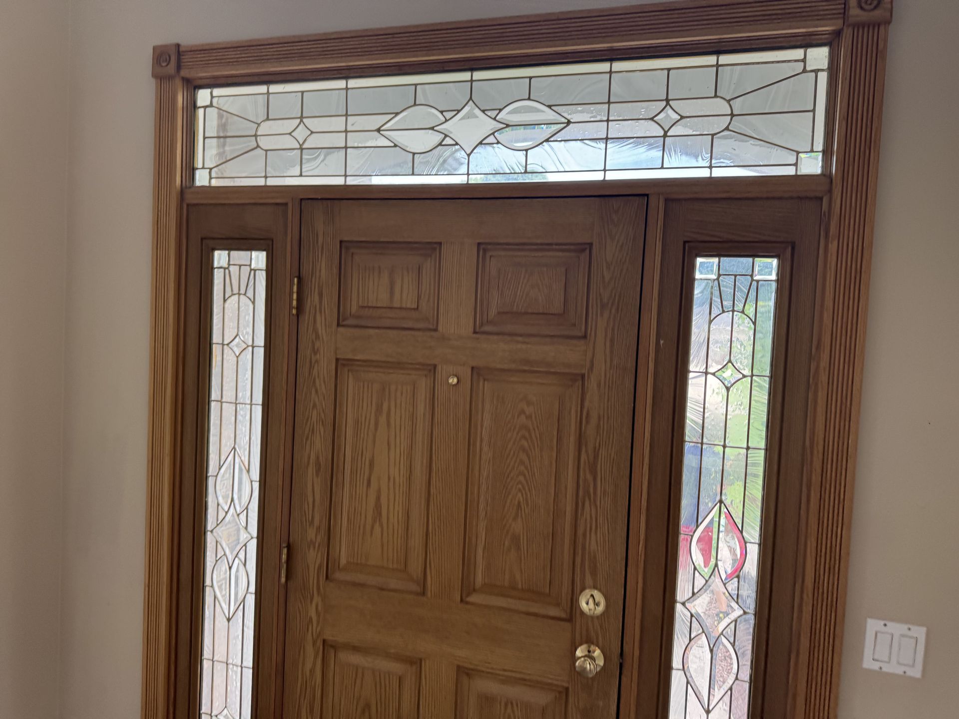 A wooden front door with stained-glass side panels and a transom window, framed by ornate, twisted-wood molding.