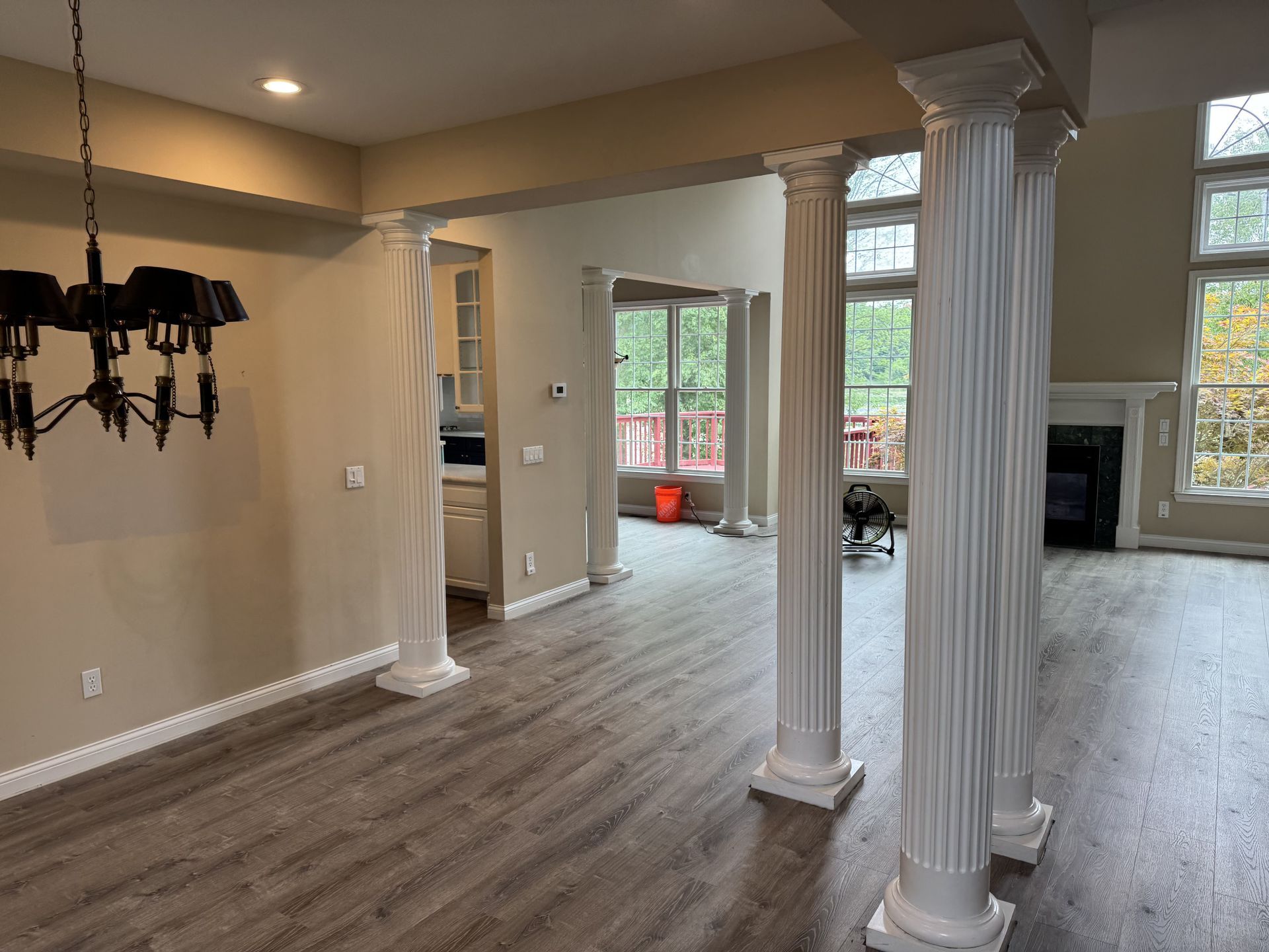A light-filled living area featuring white fluted columns, wood-look flooring, a dining chandelier, and large windows.