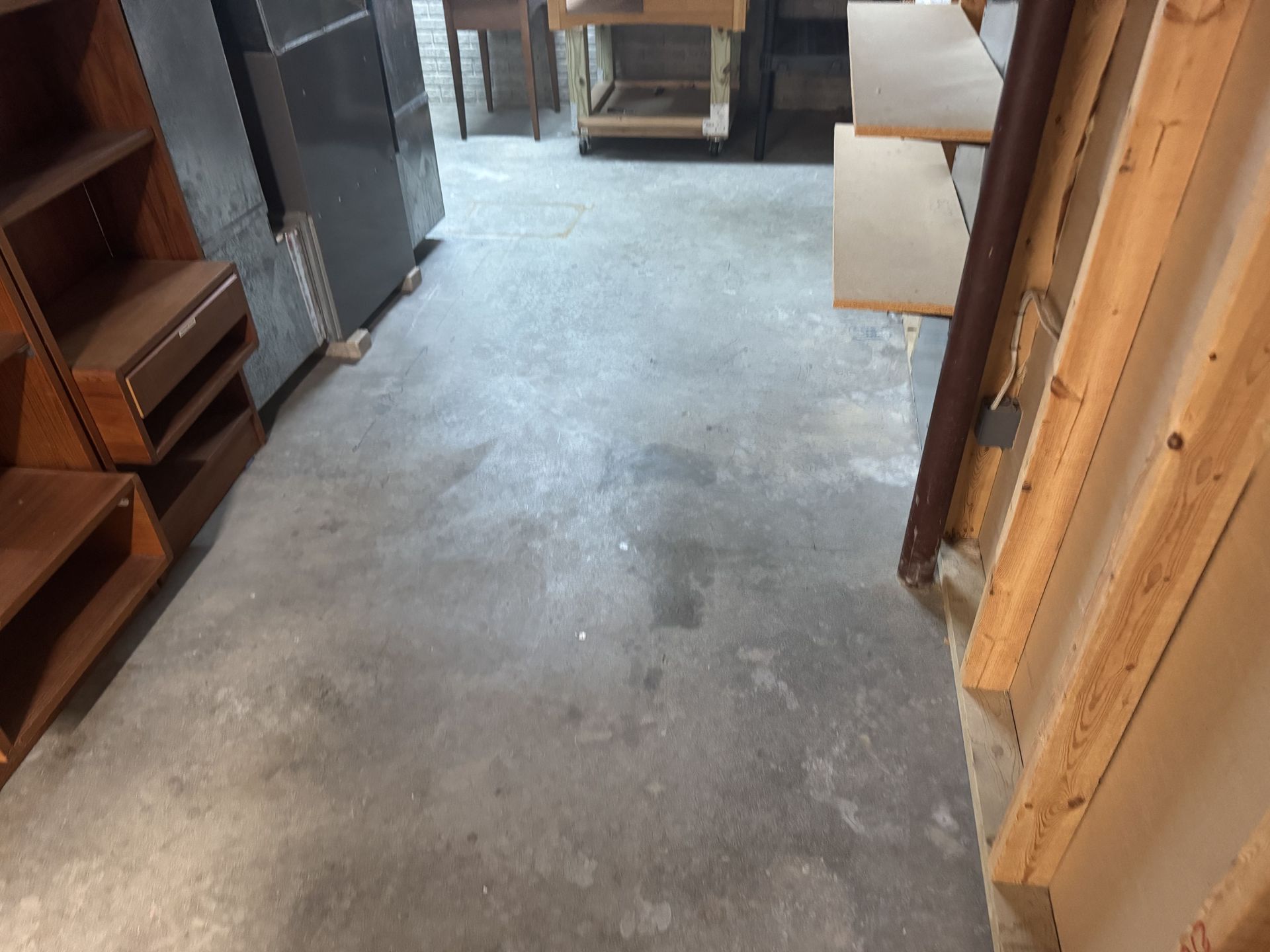 A gray concrete floor in a workshop setting, flanked by wooden shelves and unfinished structural framing.