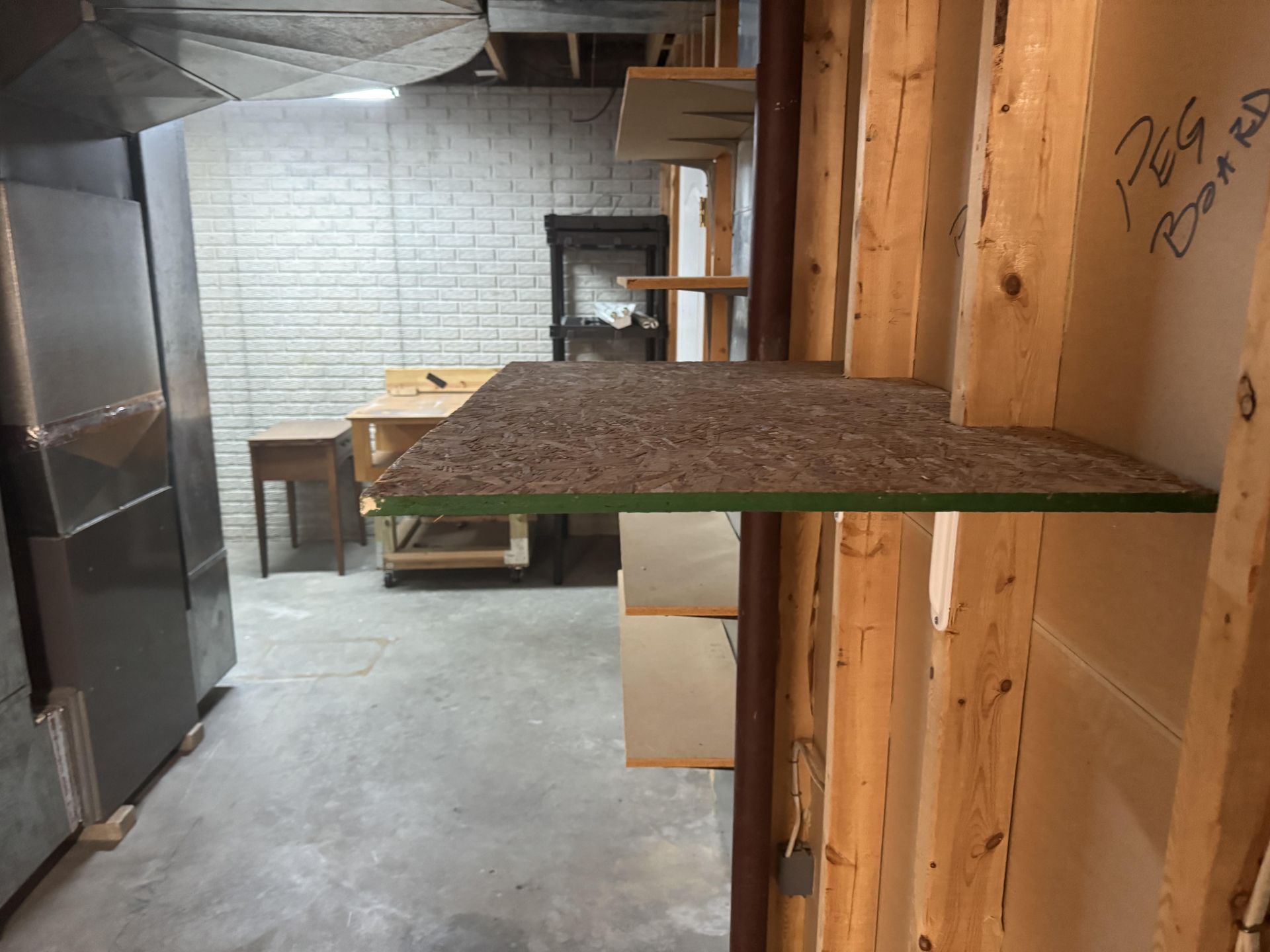 A partially finished basement with bare wooden wall studs, shelves, a small wooden side table, and a storage cabinet.
