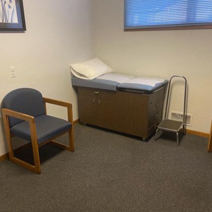 Empty medical exam room with chair, exam table, and step stool