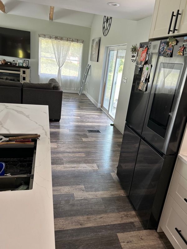 A modern open-plan home interior featuring light wood-look flooring, a kitchen island, and a dark refrigerator.