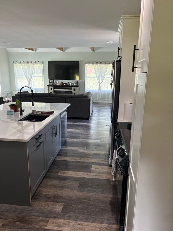 A modern kitchen featuring a dark grey island with a white countertop, leading into an open-concept living area.