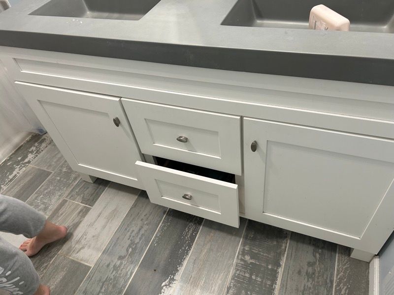 A white double-sink bathroom vanity with gray countertops and a partially opened lower center drawer.