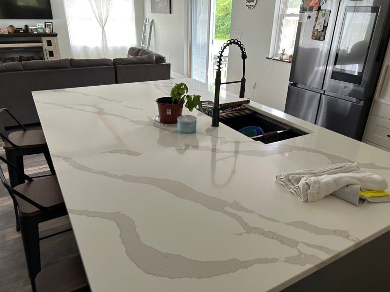 Large white quartz kitchen island with gray veining, a sink, a faucet, a potted plant, and a dish towel.