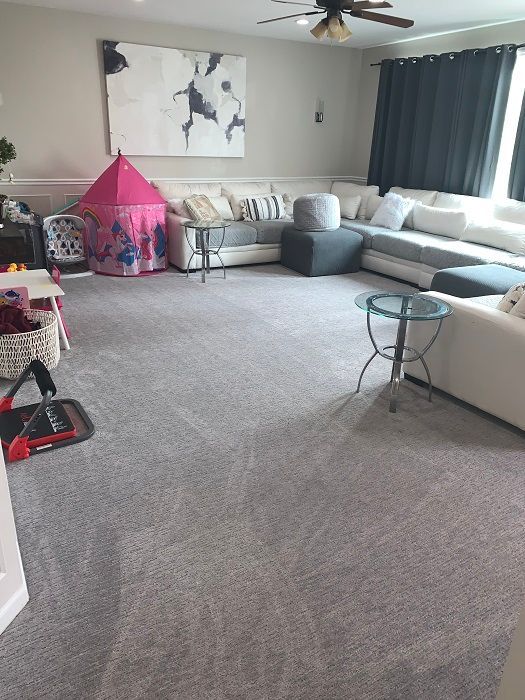 A spacious living room featuring a large grey sectional sofa, a pink play tent, and a central circular side table.