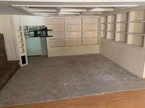 An empty room features wall-to-wall off-white built-in shelving, a coffered ceiling, and gray carpeting over wood flooring.