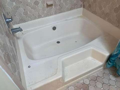 A white bathtub with a built-in step and integrated faucet, set against a tiled wall and floor with circular patterns.
