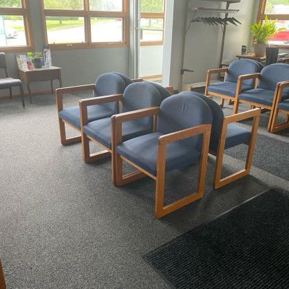 Waiting room with blue upholstered chairs, carpeted floor, and large windows.