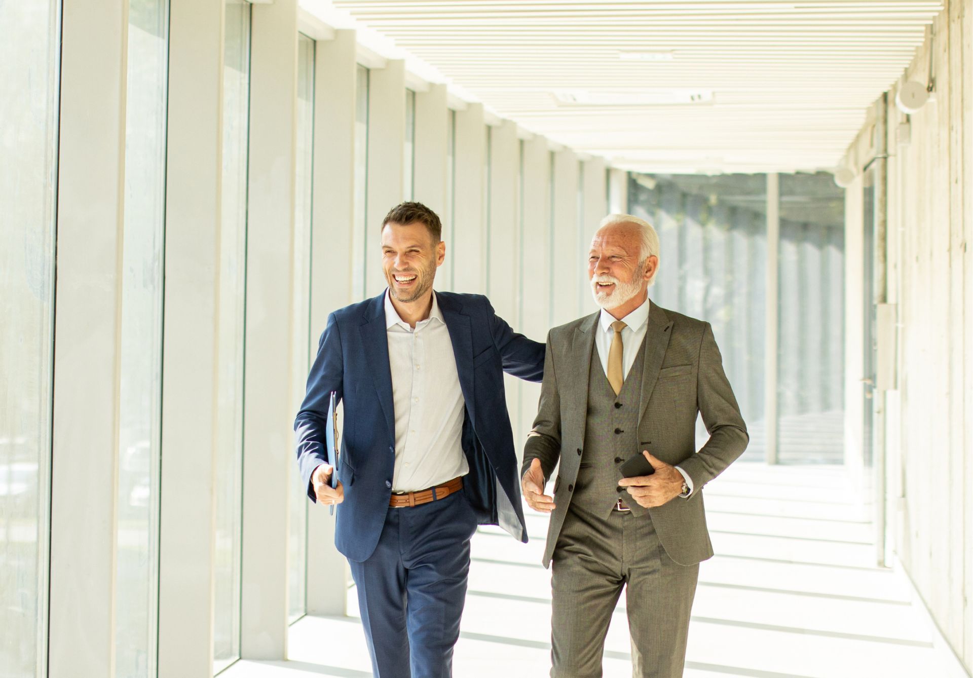 Two men in suits are walking down a hallway.