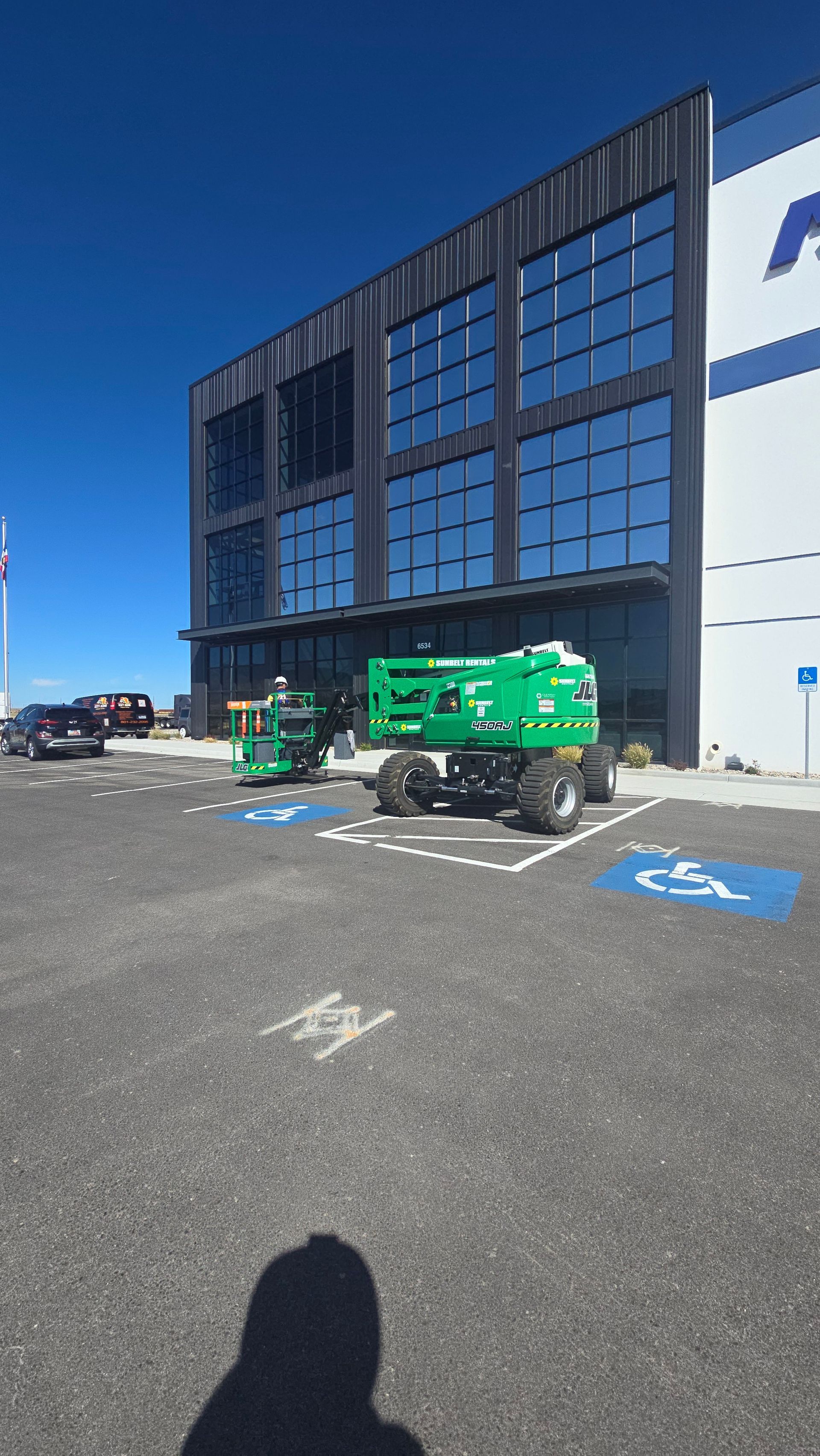 Exterior of a modern building with a green lift, a parked truck, and a blue sky.