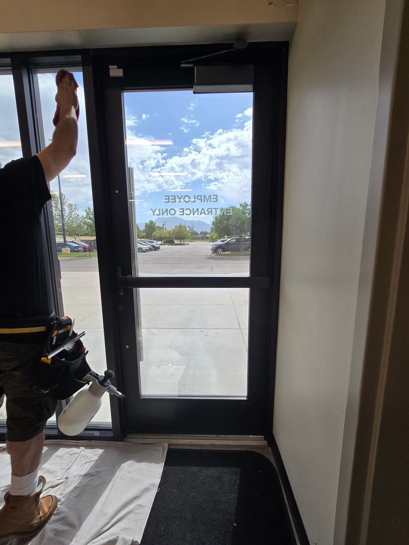 Person installing window film on a commercial door. Exterior view through the glass.