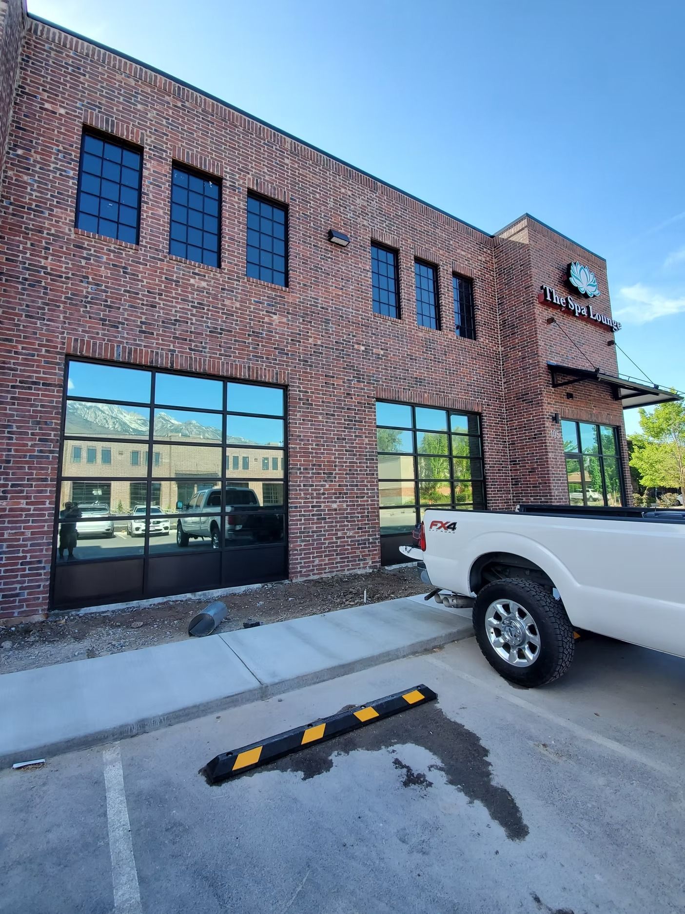 Brick building with large windows reflecting sky and a white pickup truck parked in front.