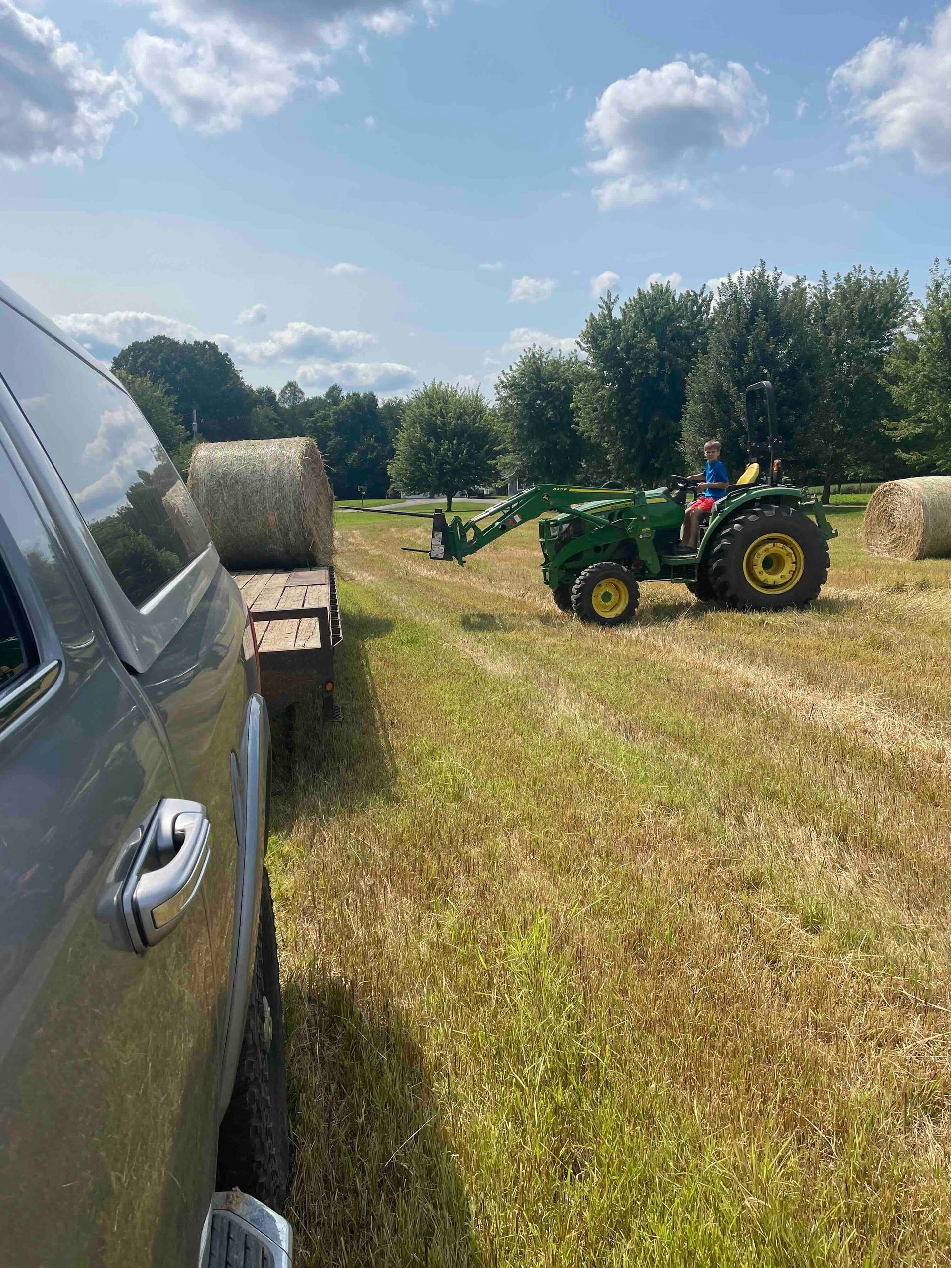 A tractor is driving through a field of hay bales.