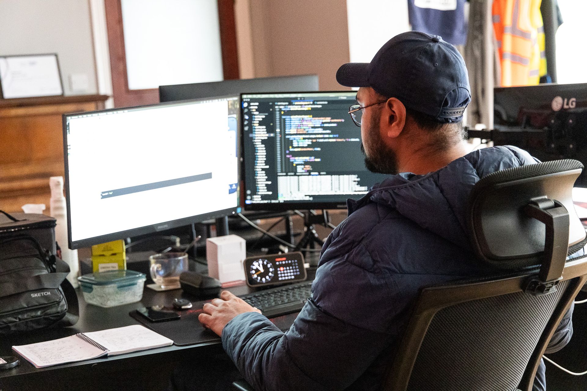 A man is sitting at a desk in front of two computer monitors.