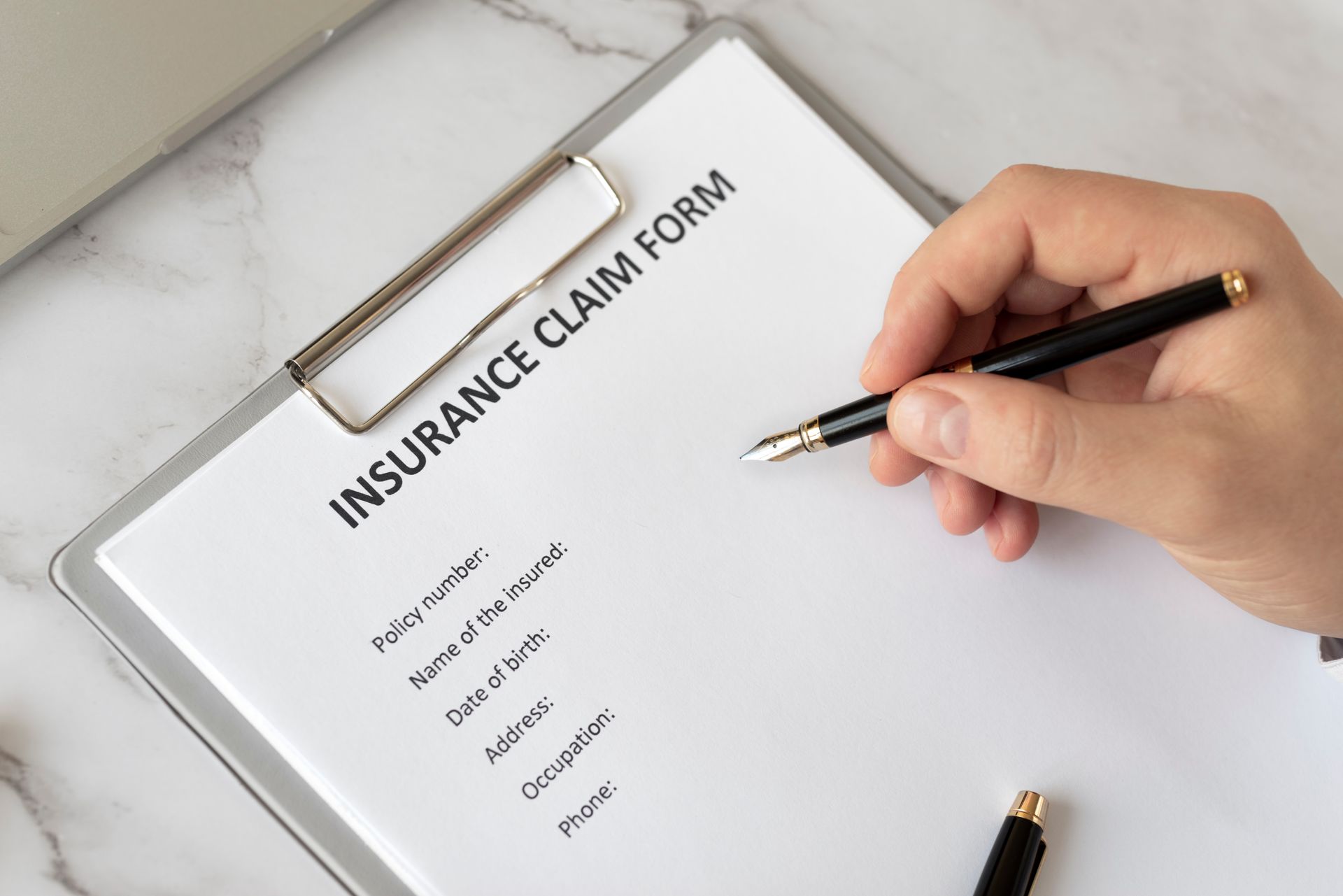 Close Up Hand Holding Pen To A Insurance Claim Form