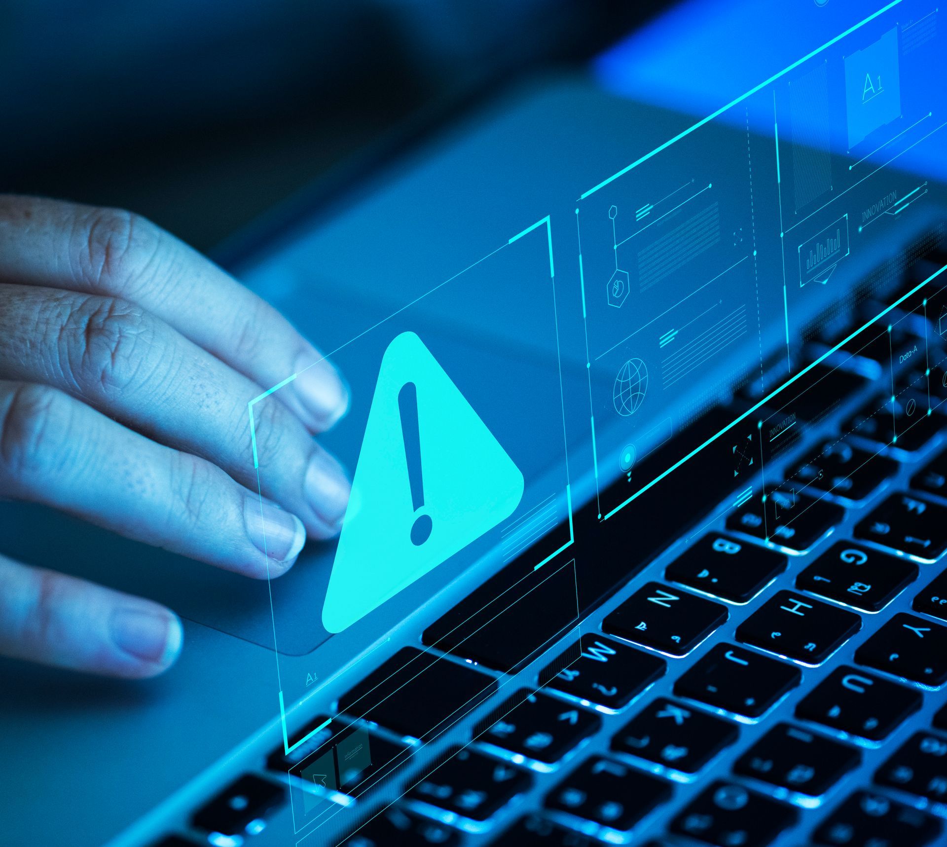 A person is typing on a laptop with a warning sign on the screen.