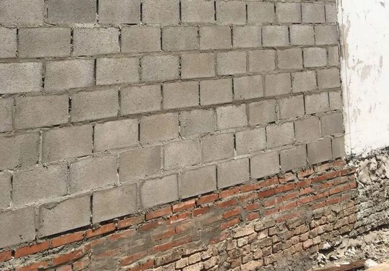 Partially plastered cinder block wall above exposed red brick base, with rough concrete floor