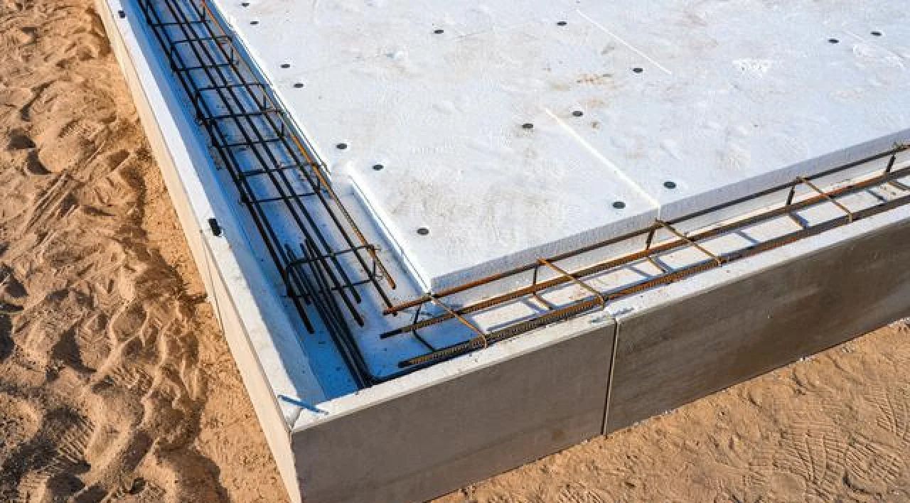 Concrete foundation corner with exposed rebar beside sand