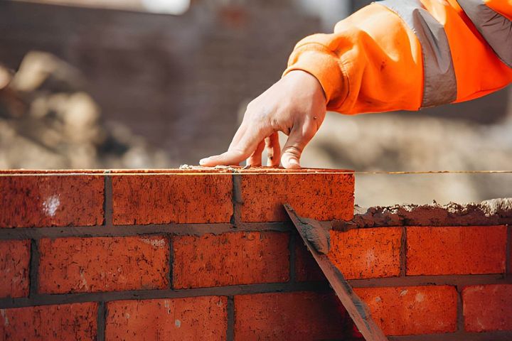 Worker in orange jacket laying red bricks on a wall at a construction site