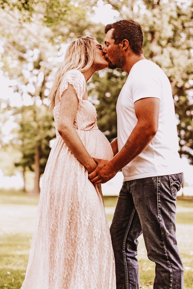 A man and a pregnant woman are kissing in a park.