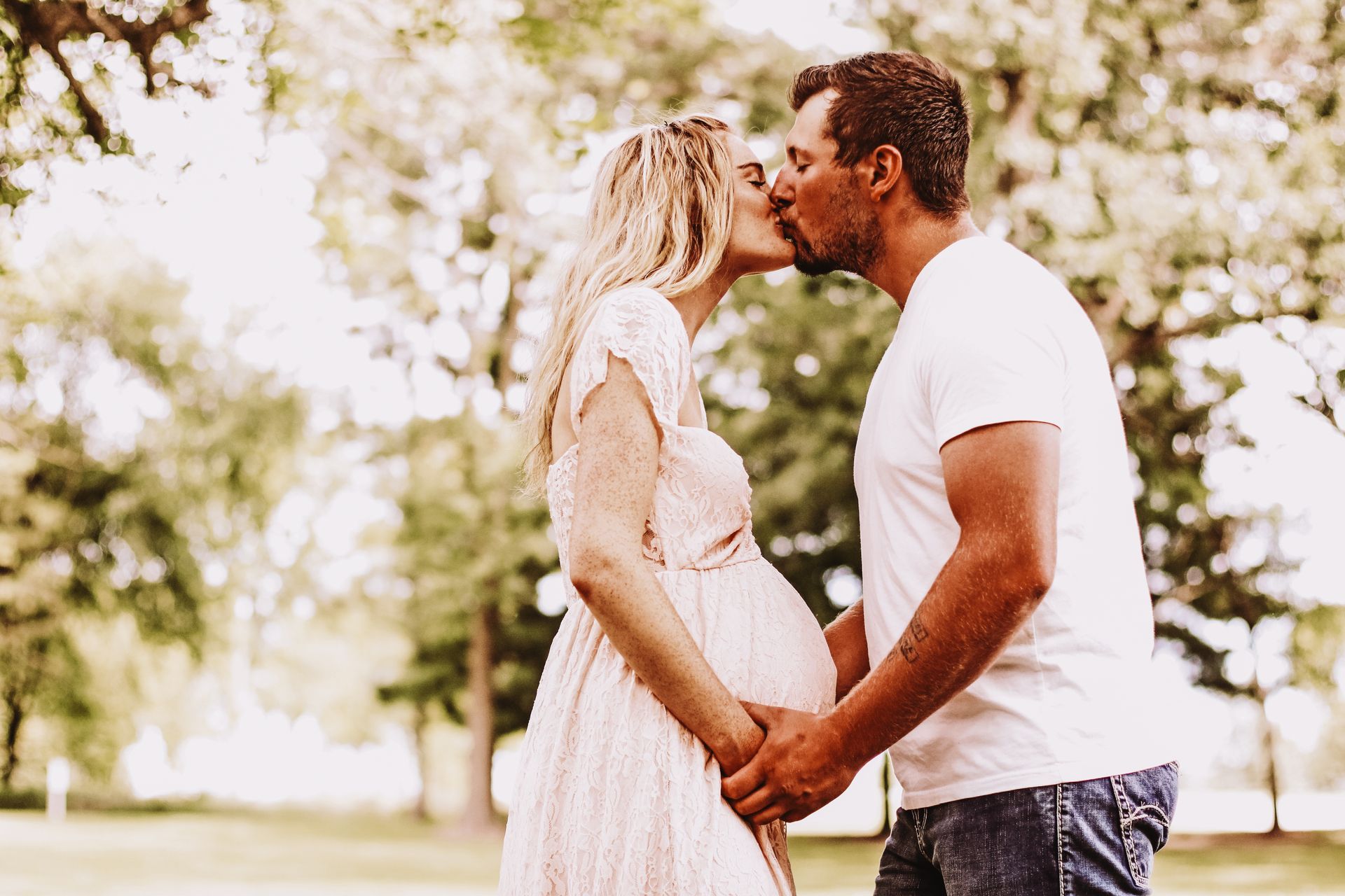 A man and a pregnant woman are kissing in a park.