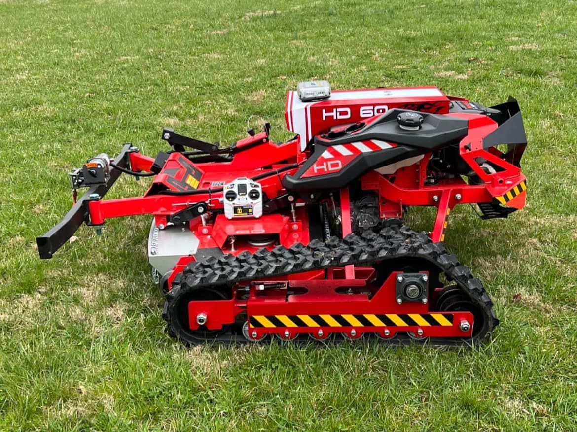 Red tracked robot on grass with black arms and hazard-striped front attachment