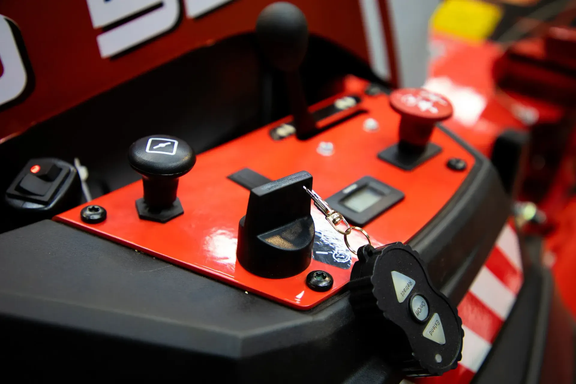 Red and black control panel with buttons, a joystick, and a small remote on a vehicle.