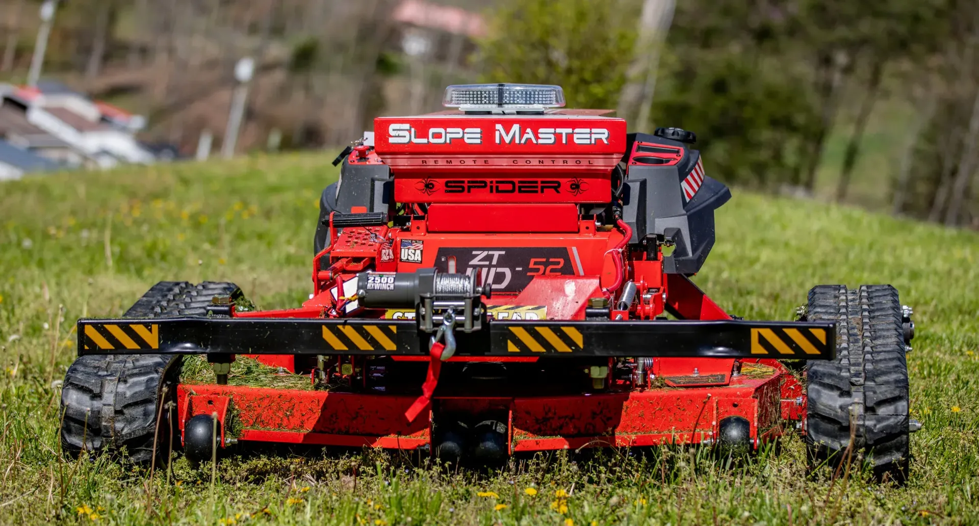 Contact Us Red robotic lawnmower, Slopemaster Spider, on a grassy slope. It has treads and flashing light on top.