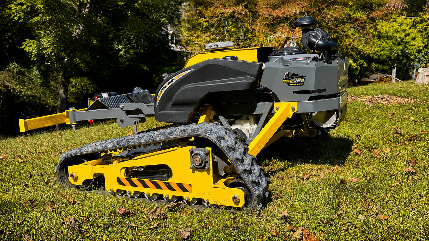 Yellow-and-black tracked mini excavator on grass, with arm extended in a wooded outdoor area
