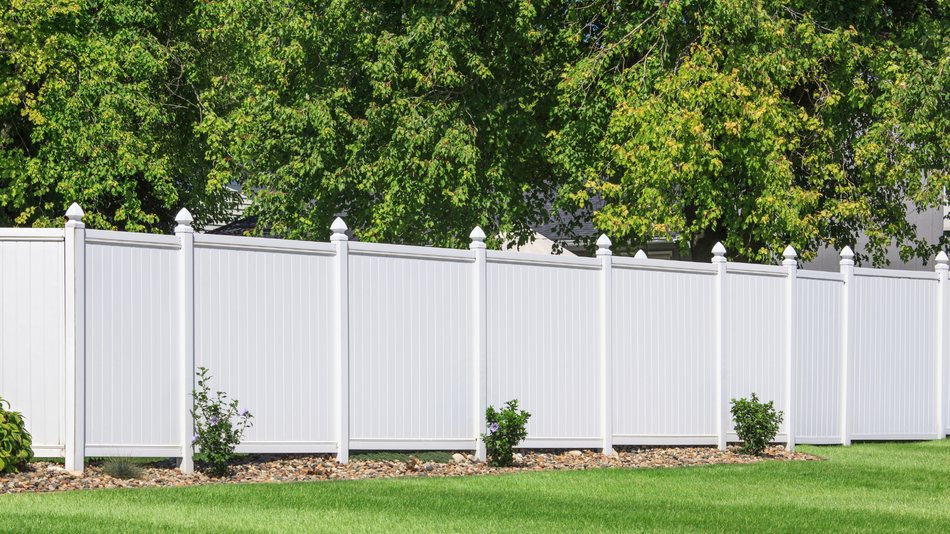 White vinyl fence in front of green lawn and trees.
