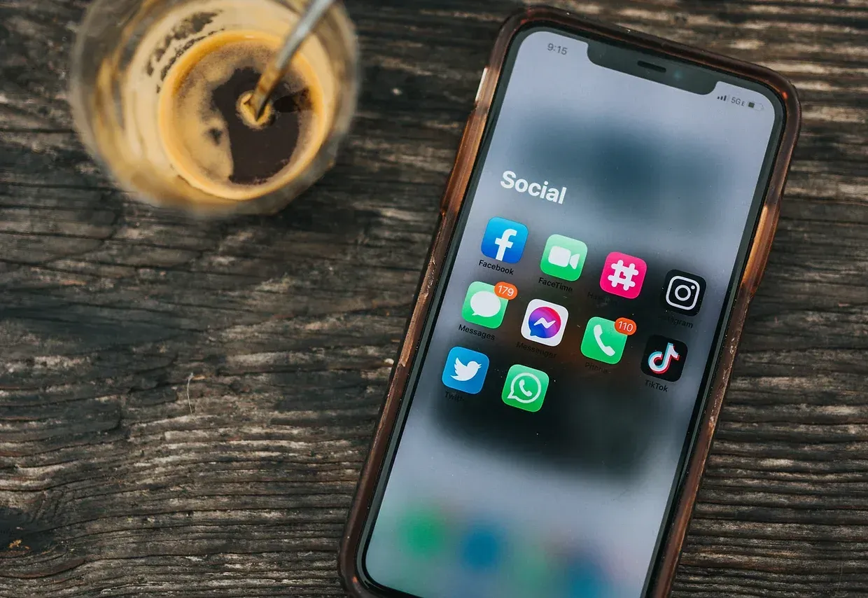 A cell phone is sitting on a wooden table next to a cup of coffee.