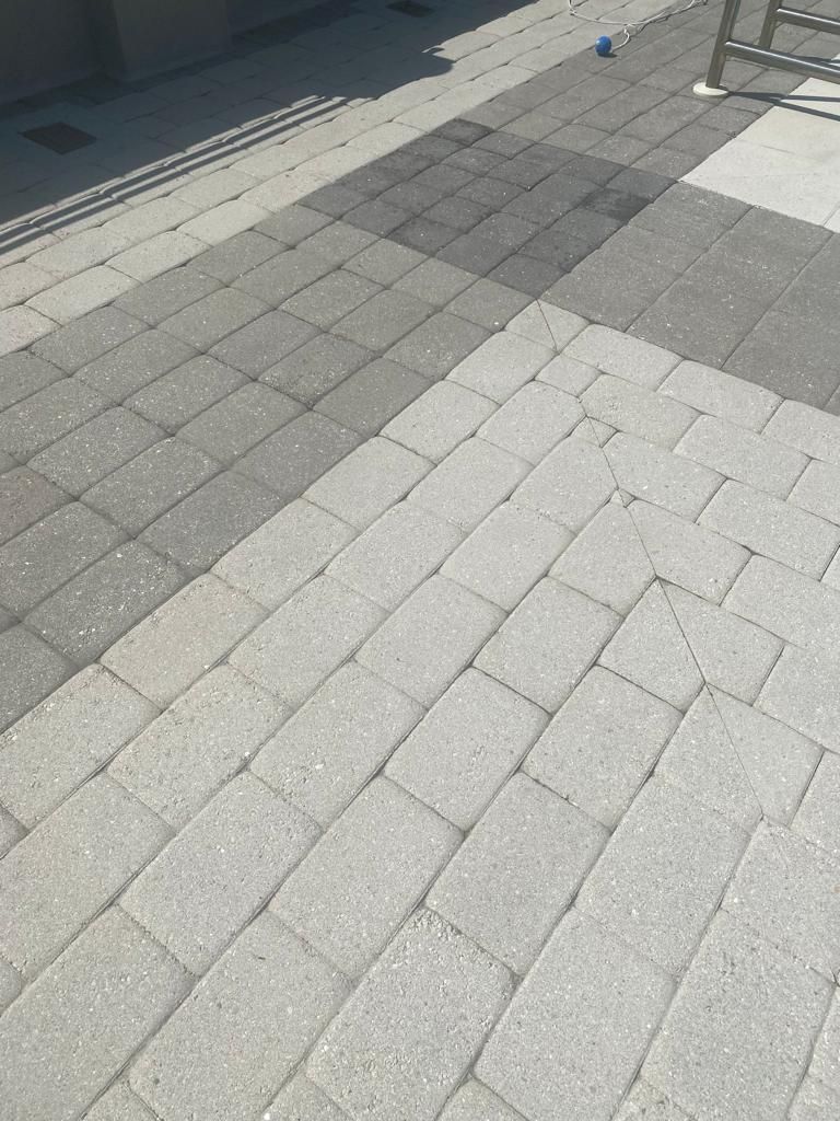 Paved patio with rectangular light gray bricks. A diagonal pattern leads to a darker gray section and a gray sidewalk.