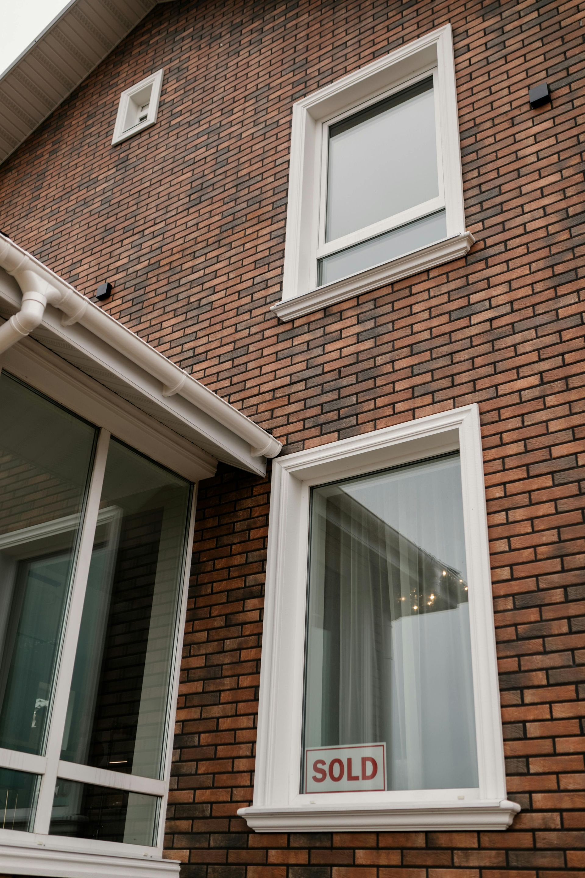 Brick house exterior with white-framed windows, one displaying a