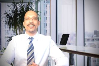 Smiling man in a white shirt and striped tie in an office with a laptop and plants in the background